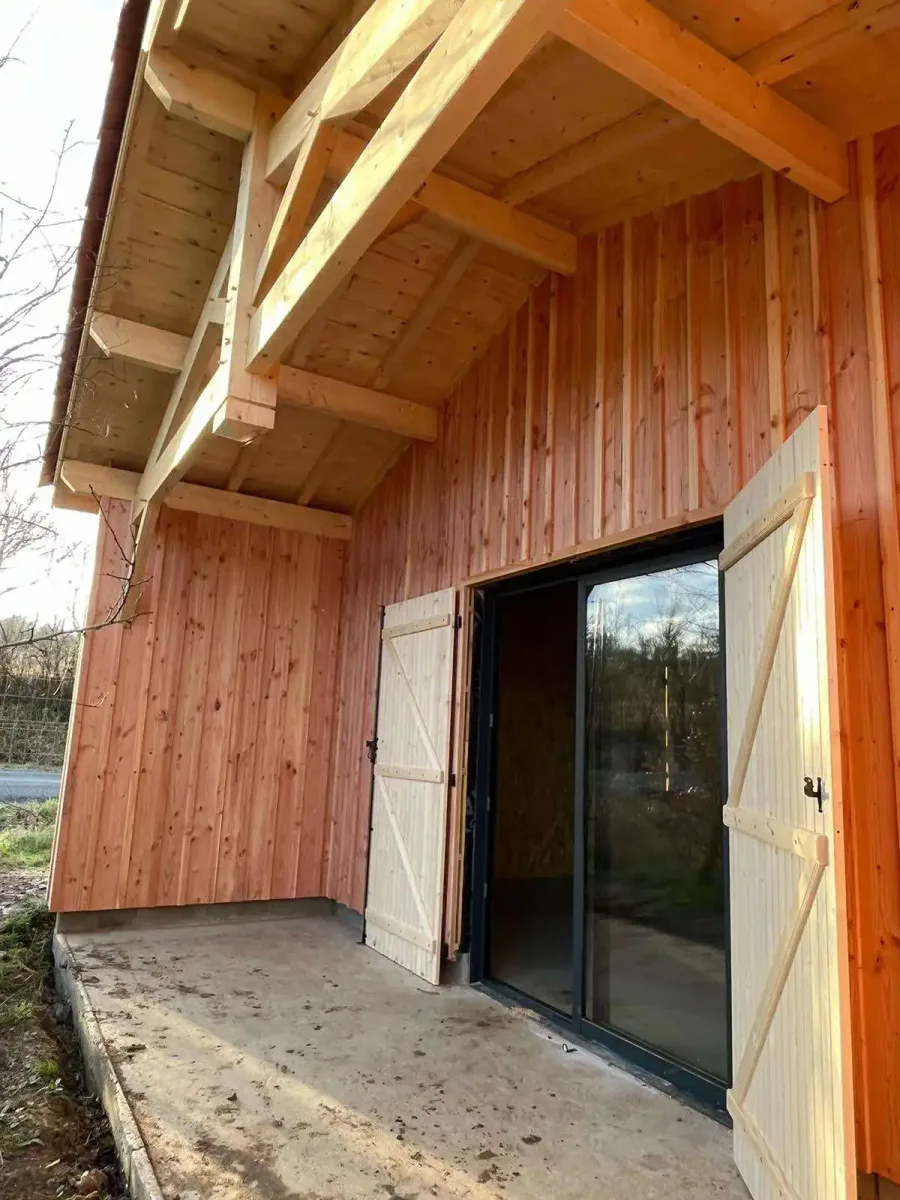 Bâtiment à ossature bois avec bardage vertical, baie vitrée et volets en bois
