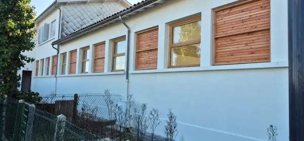 Façade habillée de bardage bois entre les fenêtres, avec descente d'eaux pluviales en zinc