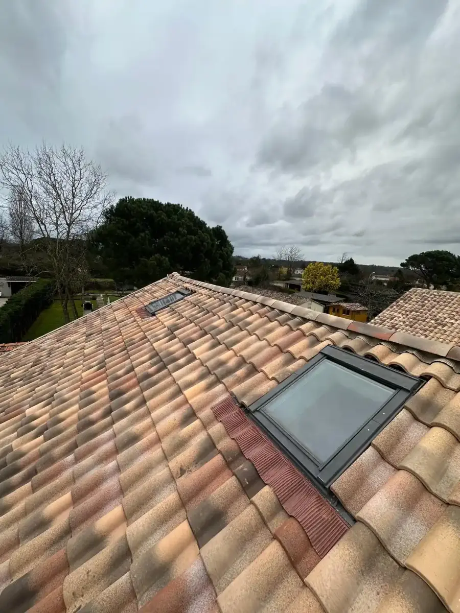 Toiture en tuiles rénovée équipée d'une fenêtre de toit, sous un ciel couvert