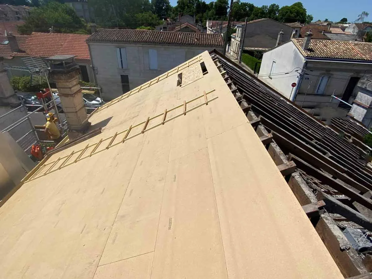 Panneaux isolants posés sur la charpente d'une toiture en cours de sarking, avec échelle de couvreur
