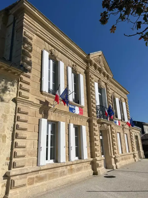Façade d'une mairie en pierre de taille, pavoisée aux couleurs françaises et européennes