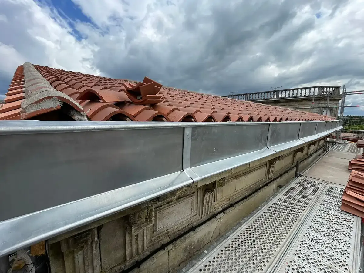 Chéneau en zinc neuf posé en pied de toiture le long d'une balustrade en pierre