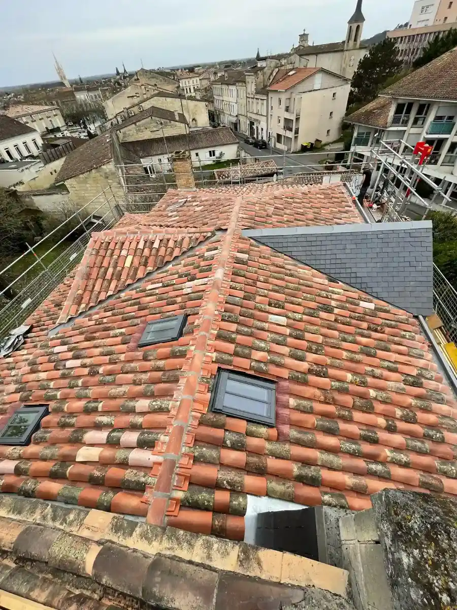 Vue plongeante sur une toiture en tuiles restaurée équipée de fenêtres de toit, dominant un village girondin